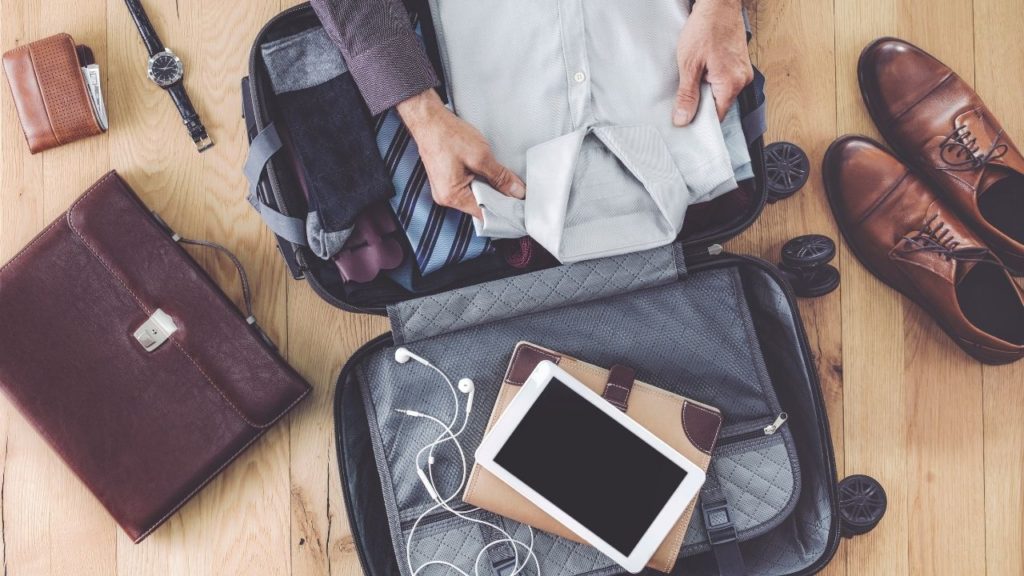 Shoes, I Pad, shirt, tie, watch, wallet, and briefcase neatly displayed in luggage on on the floor as a man packs his luggage.