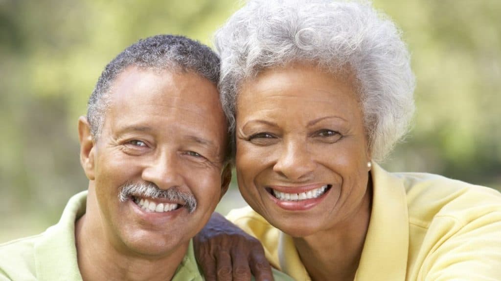 Couple smiling taking a photo outside together. He is wearing a green shirt and she is wearing a yellow shirt.