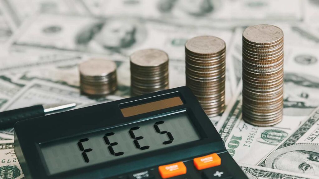 Calculator with fees written on it, coins stacked in row with hundred dollar bills below