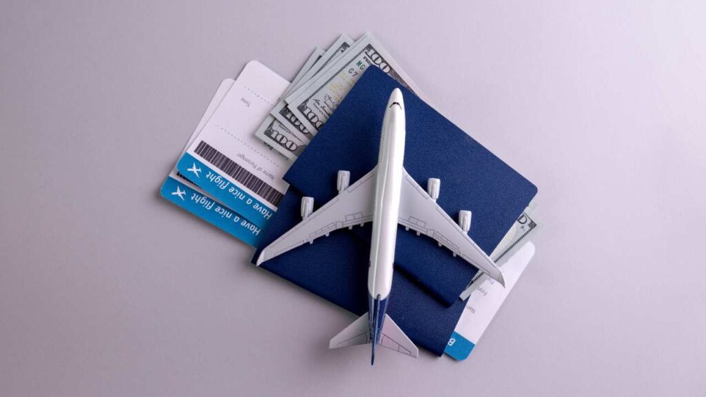 A toy airplane on top of 2 passports, 2 plane tickets, and some cash