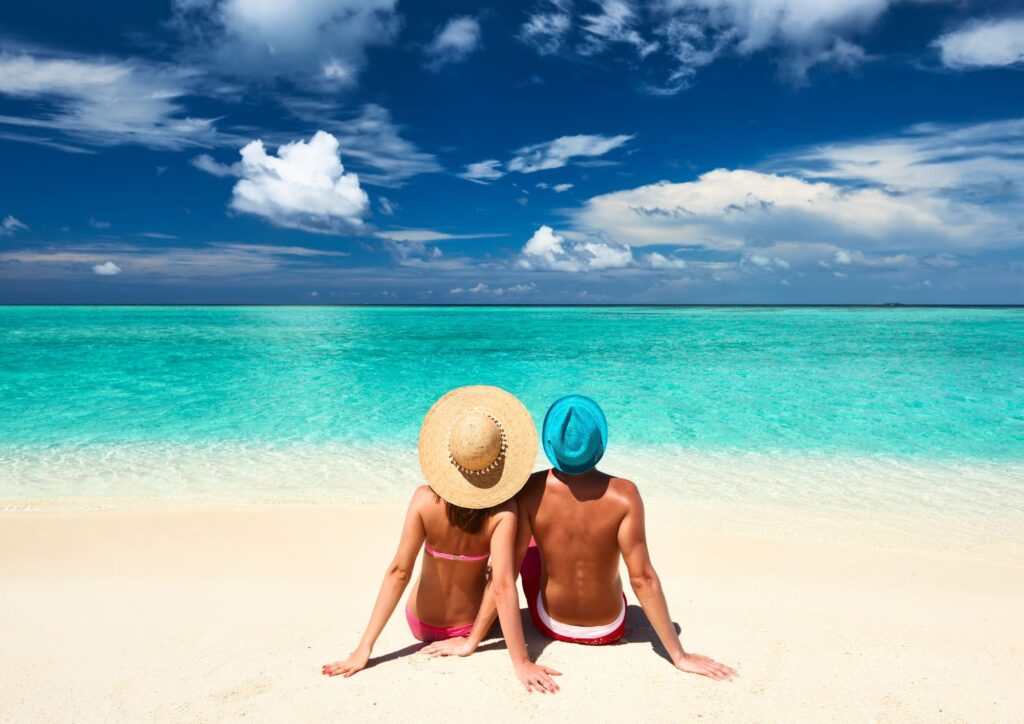 A couple sitting on the beach looking at the blue water - Where to stay in Aruba for couples